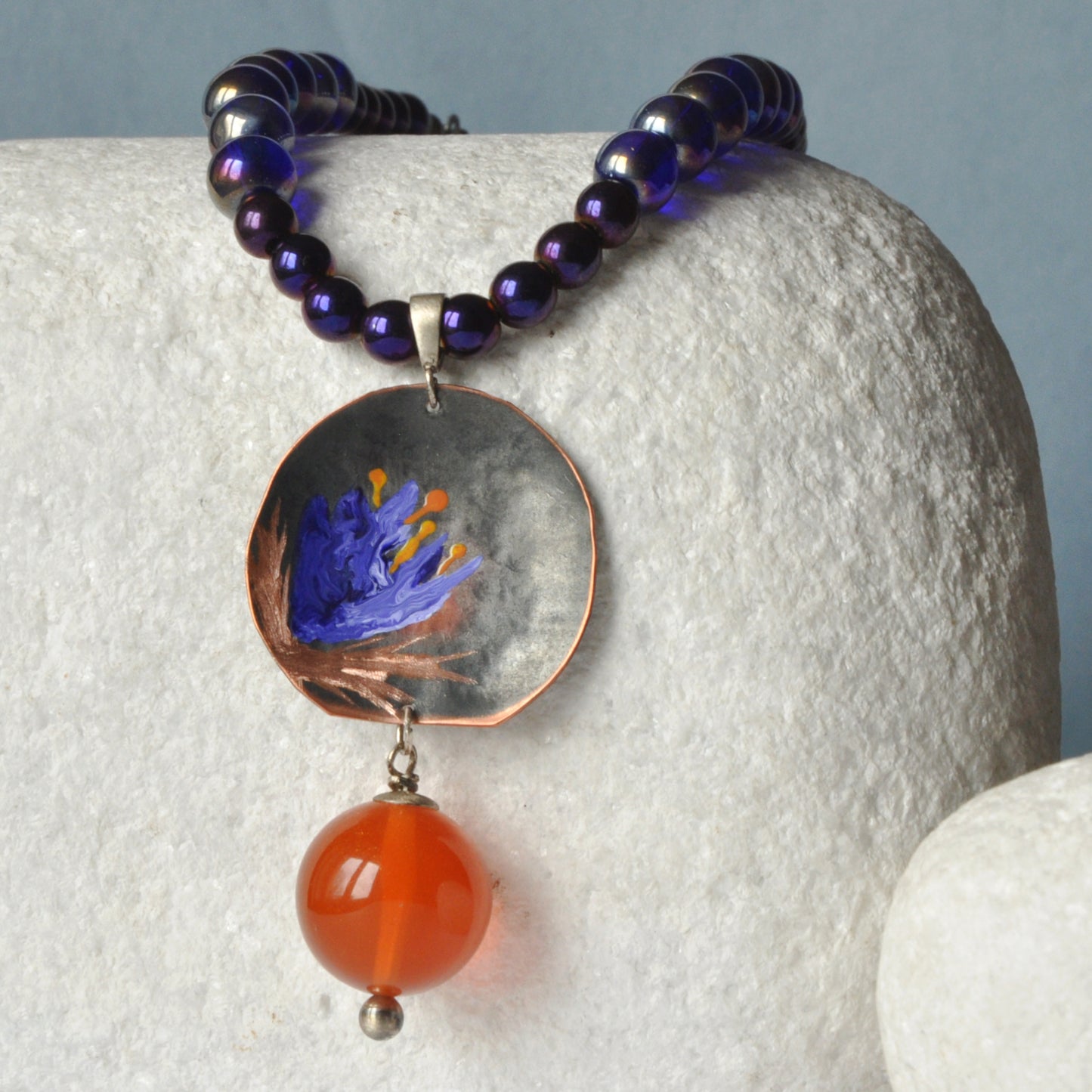 Necklace with patinated hand-forged & engraved copper pendant with enameled flower and orange resin smooth ball 'Dark Blue Lily'